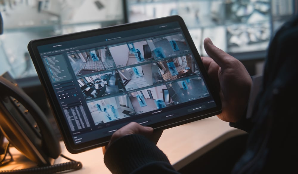 Man holding tablet that shows security feeds from different business cameras
