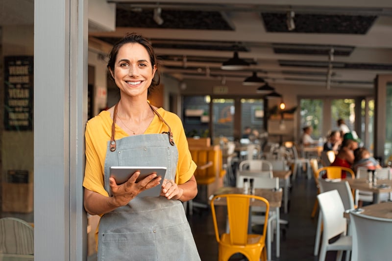 Small business owner outside her doors with tablet and smiling face